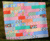 Quick and easy PDF quilt pattern with colorful floral patchwork and strip piecing displayed outdoors on a rustic fence.
