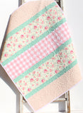 Easy strip quilt pattern featuring diagonal sashing and mixed floral, plaid, and geometric fabrics in a modern handmade baby quilt.