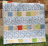 Charm square baby quilt featuring playful train fabrics and modern strip piecing in a beginner-friendly nursery quilt pattern.