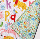 Handmade alphabet quilt for babies with animals and letters, embroidered name option, colorful nursery blanket design.