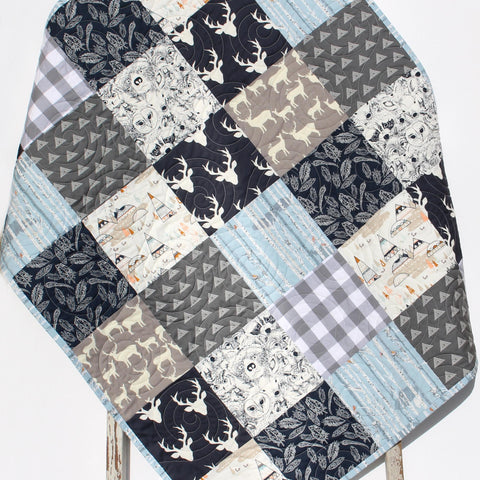 Handmade woodland patchwork quilt with embroidered name, featuring forest animals, deer, trees, and soft neutral fabrics.