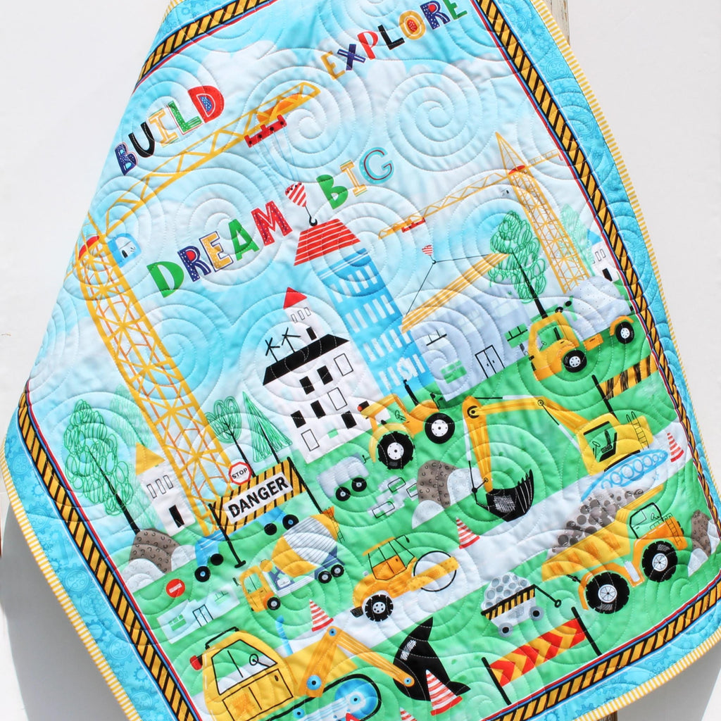 Personalized construction baby quilt with dump truck, bulldozer, and crane prints, embroidered name detail, and handmade heirloom quality.