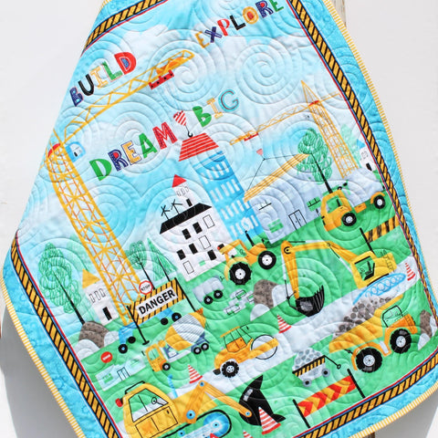 Personalized construction baby quilt with dump truck, bulldozer, and crane prints, embroidered name detail, and handmade heirloom quality.