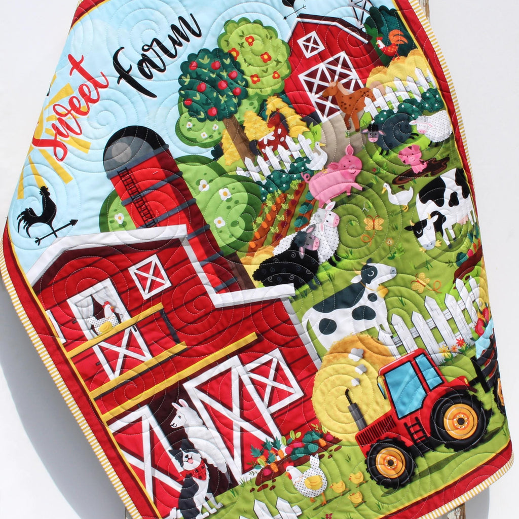 Personalized farmyard baby quilt with red barn, tractors, cows, pigs, and embroidered monogram on soft cotton fabric.