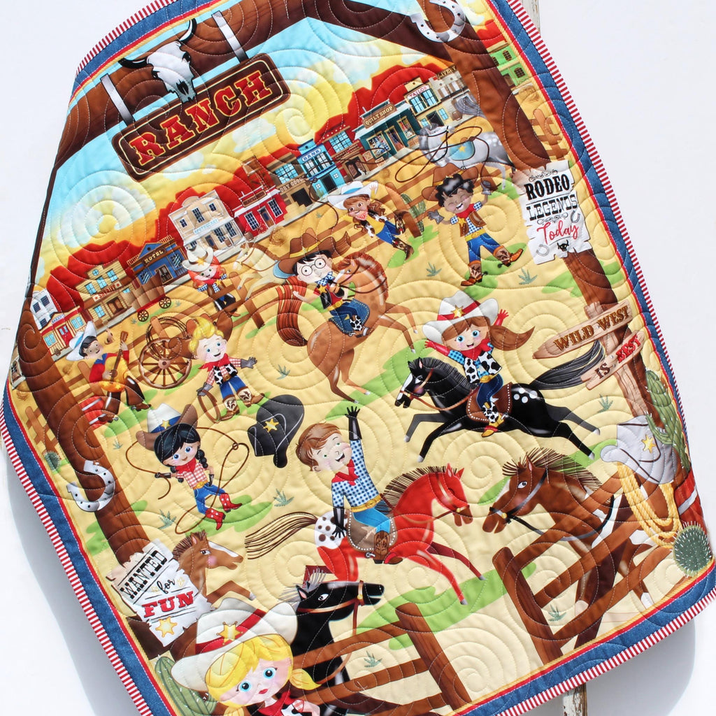 Handmade personalized cowboy baby quilt with embroidered name, featuring rodeo cowboys, horses, and rustic Wild West fabric prints.