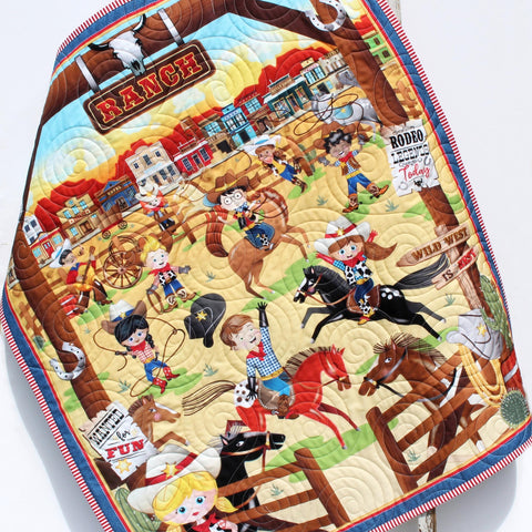 Handmade personalized cowboy baby quilt with embroidered name, featuring rodeo cowboys, horses, and rustic Wild West fabric prints.