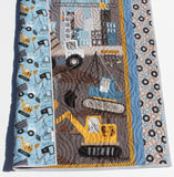 Baby boy construction quilt with coordinating blue and gray borders, featuring excavators and trucks, designed by Kristin Blandford Designs for modern nursery bedding and baby gifts
