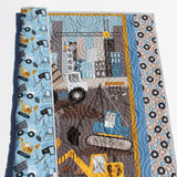 Close-up of construction quilt panel with excavator and dump truck design, quilted swirl stitching detail, handmade by Kristin Blandford Designs for baby nursery decor